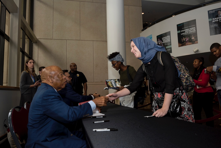 Congressman John Lewis sits at a table where he is signing books for audience members at George Mason University who heard him speak. He shakes hands with a Mason student, who is standing on the other side of the table.